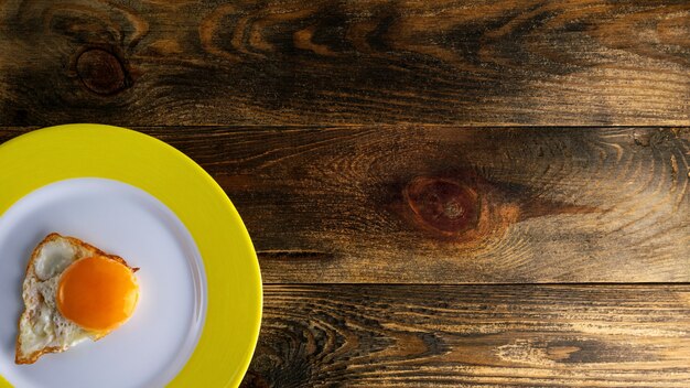 Gema frita em prato redondo de cerâmica com borda amarela em superfície áspera de madeira