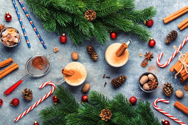 Gemada quente de inverno ou coquetel de outono com ovos de leite e rum escuro polvilhado com canela e noz-moscada em copos de vidro em fundo cinza mesa de Natal definindo vista superior