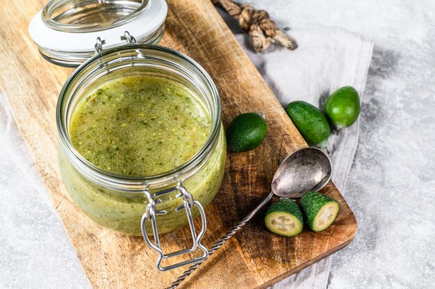 Gemahlene grüne Feijoa mit Zucker auf einem hölzernen Schneidebrett in einem Glas. Grauer Hintergrund. Draufsicht.