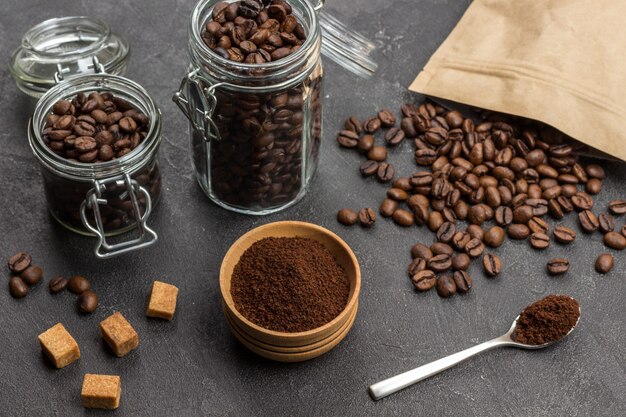 Gemahlener kaffee in holzschale und löffel. geröstete kaffeebohnen im glas und in der papiertüte. stücke brauner zucker auf dem tisch. draufsicht.