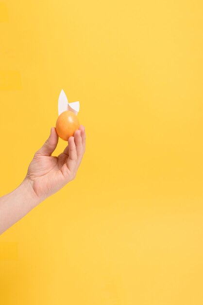 Gemalte bunte Eier in der Hand mit Hasenohren für gelben Hintergrund des Osterfeiertags.