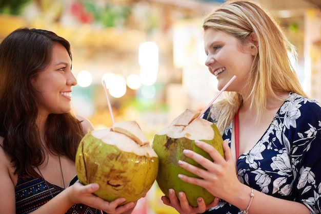 Gemeinsam auf drei Schnappschuss von zwei jungen Frauen, die in einem ausländischen Lebensmittelgeschäft aus Kokosnüssen trinken