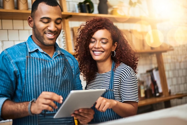 Gemeinsam auf großartige Ideen kommen Schnappschuss eines liebevollen jungen Paares, das in seinem Café an einem Tablet arbeitet