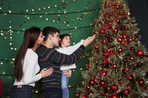 Gemeinsam die Feiertage genießen. Glückliche Familie, die neues Jahr feiert und nahe Weihnachtsbaum steht.