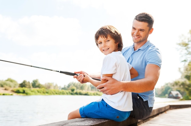 Gemeinsam fischen macht Spaß. Fröhlicher Vater und Sohn, die zusammen angeln, während der kleine Junge in die Kamera schaut und lächelt