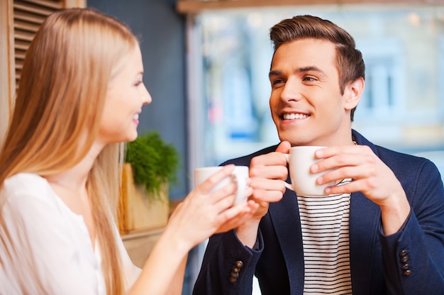 Gemeinsam frischen Kaffee genießen. Schönes junges Paar, das miteinander spricht und lächelt, während es zusammen Kaffee im Café genießt?