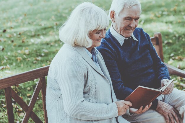 Gemeinsam ihr Lieblingsbuch genießen. Fröhliches älteres Paar, das zusammen ein Buch liest, während es auf der Parkbank sitzt