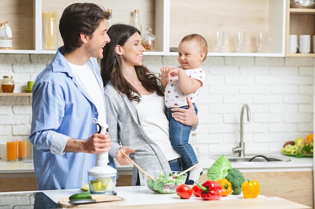 Gemeinsam kochen. Mama macht Salat für Erwachsene, Papa macht Apfelpüree für Babysohn in der Küche, leerer Raum