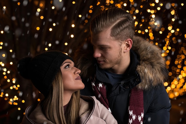 Gemeinsam Spaß bei einer Weihnachtsfee haben Junges fröhliches Paar macht einen Spaziergang und genießt es, warm gekleidet zu sein, einander anzusehen und zu lachen