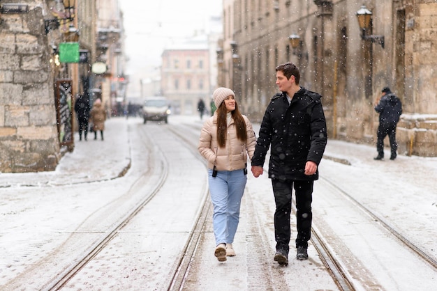 Gemeinsam Spaß haben bei einer Weihnachtsfee mit Schneefall Junges fröhliches Paar macht einen Spaziergang und genießt es, warm gekleidet zu sein, einander anzusehen und überall Schneeflocken zu lachen