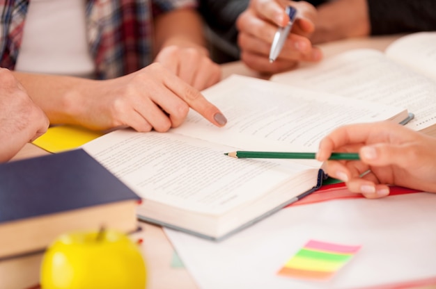 Gemeinsam studieren. Nahaufnahme von Schülern, die auf ein Buch zeigen, während sie zusammen am Schreibtisch sitzen