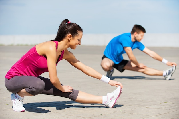 Gemeinsames Training macht Spaß. Schöne junge Frau und Mann, die zusammen Dehnübungen machen, während sie im Freien stehen