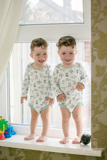 Gemelos alegres - hermanos de pie en el alféizar de una ventana