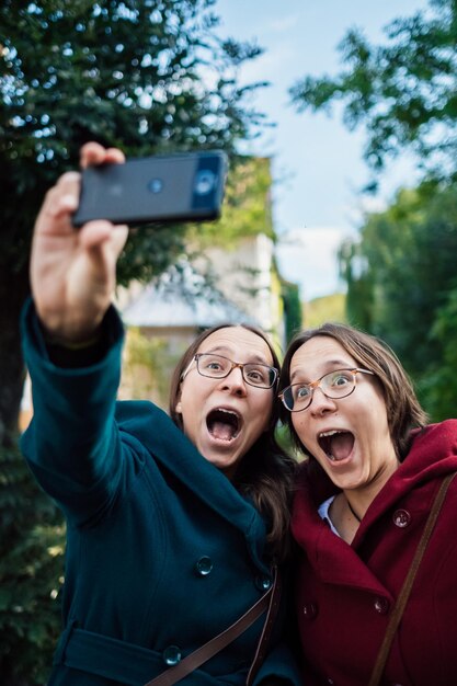 Foto gemelos haciendo caras mientras se toman selfies con teléfonos inteligentes