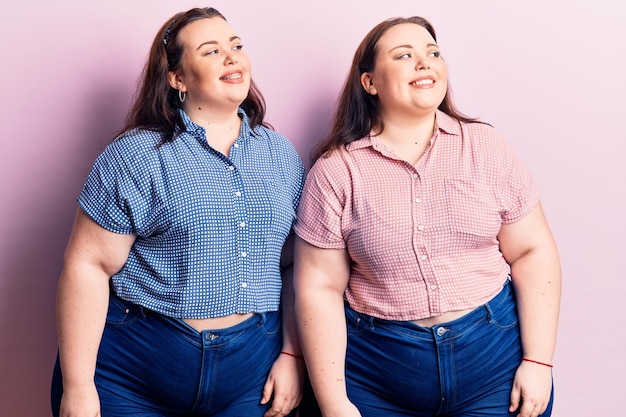 Gemelos jóvenes de talla grande con ropa informal mirando de un lado a otro con una sonrisa en la cara expresión natural riendo confiados