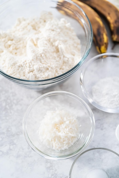 Gemessene Zutaten in Rührschüsseln aus Glas, um Kokosnuss-Bananen-Pfannkuchen zum Frühstück zuzubereiten