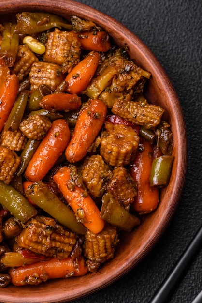 Gemisch aus Gemüse, Mais, Karotten, Pfeffer, Brokkoli, Zwiebeln in Teriyaki-Sauce auf einer Keramikplatte auf einem dunklen Beton-Hintergrund