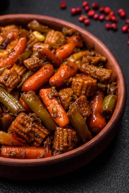 Gemisch aus Gemüse, Mais, Karotten, Pfeffer, Brokkoli, Zwiebeln in Teriyaki-Sauce auf einer Keramikplatte auf einem dunklen Beton-Hintergrund