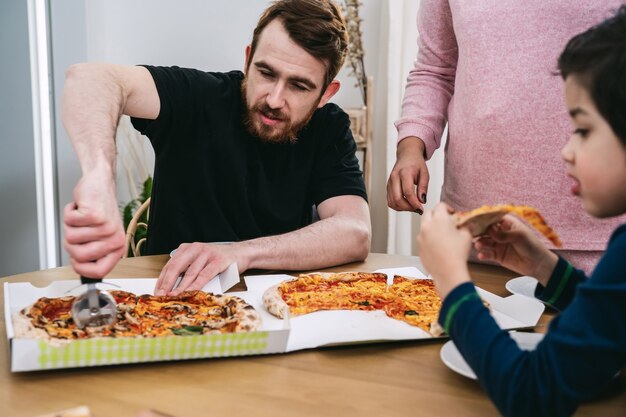 Gemischte Familie, die vegane Pizza mit natürlichen Zutaten zu Hause isst. Veganes Essen. Vielfalt und echte Menschen