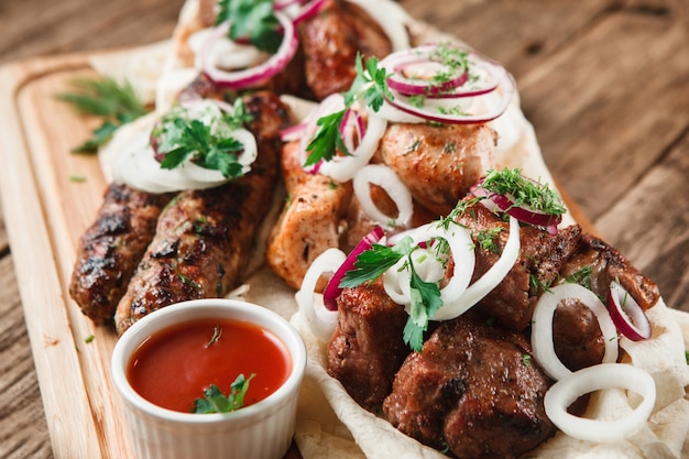 Gemischte gegrillte Fleischplatte. Verschiedenes köstliches gegrilltes Fleisch serviert auf Pitta-Brot mit Kräutern, Zwiebeln und Tomatensauce, Detailansicht.