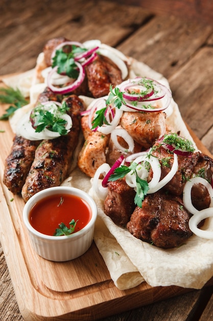 Gemischte gegrillte fleischplatte. verschiedenes köstliches grillfleisch serviert auf pittabrot mit kräutern, zwiebeln und tomatensauce.