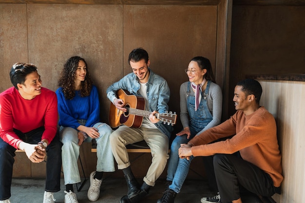 Gemischte Gruppe junger Freunde, die Zeit miteinander verbringen und gerne Gitarre spielen und singen