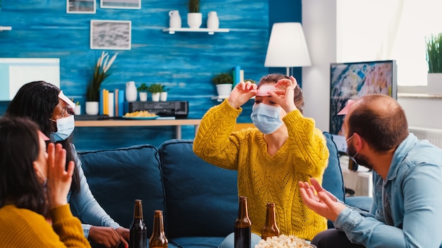 Gemischte Rassen-Freunde, die Spaß beim Spielen mit Haftnotizen auf der Stirn haben, Bier trinken und eine neue normale Party genießen