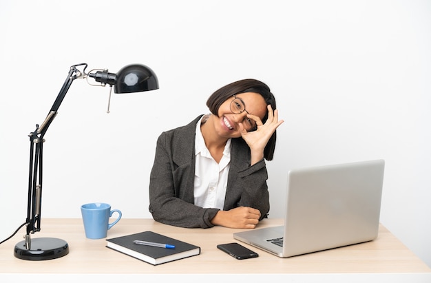 Gemischte Rassenfrau des jungen Geschäfts, die im Büro arbeitet, das ok Zeichen mit den Fingern zeigt