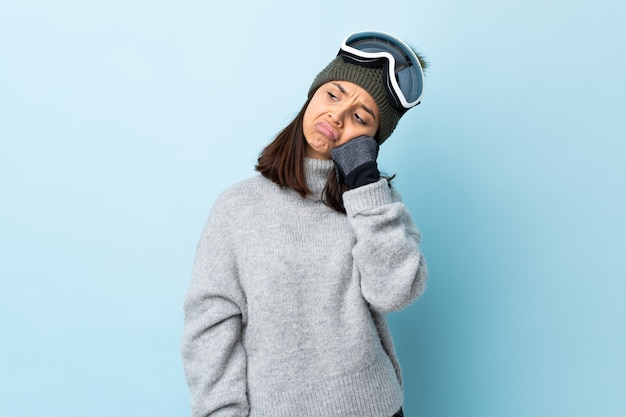 Gemischte Renn-Skifahrerin mit Snowboardbrille über isoliertem blauem Hintergrund mit müdem und gelangweiltem Ausdruck