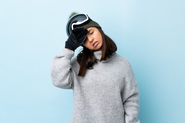 Gemischte Rennskifahrerin mit Snowboardbrille über isolierter blauer Wand mit müdem und krankem Ausdruck.