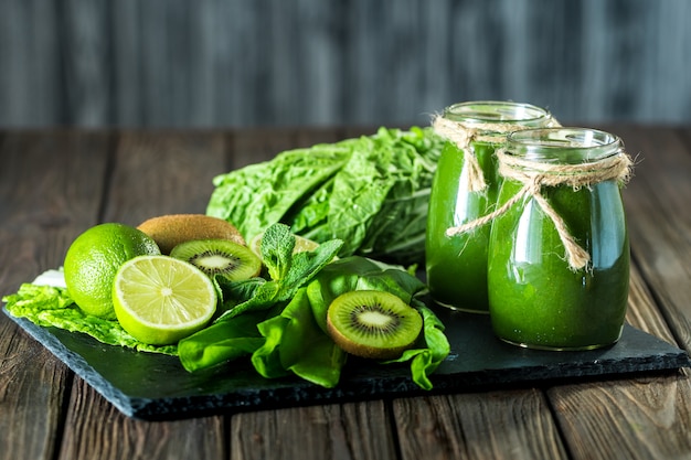 Gemischter grüner Smoothie mit Bestandteilen auf dem Steinbrett, Holztisch