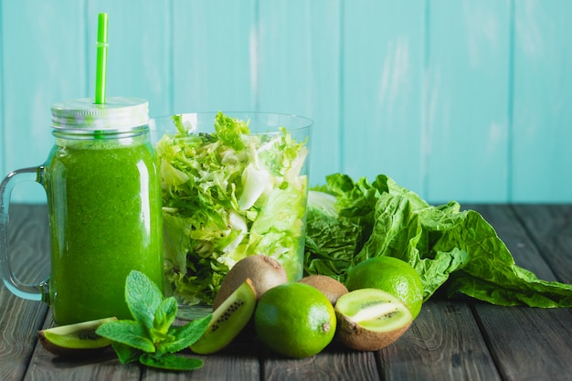 Gemischter grüner Smoothie mit Bestandteilen auf Holztisch