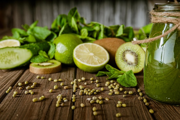 Gemischter grüner Smoothie mit Zutaten auf dem Holztisch. Grüner Cocktail. Gesunde Ernährung