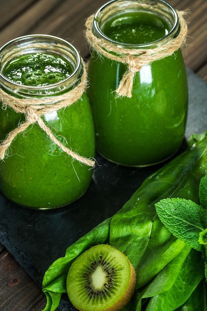 Gemischter grüner Smoothie mit Zutaten auf dem Steinbrett, Holz