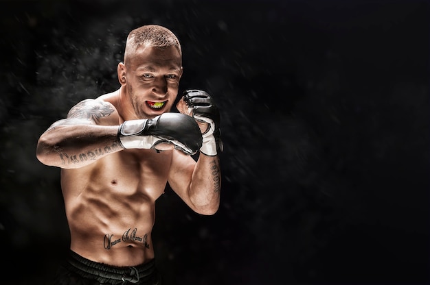 Gemischter Kampfkünstler, der auf einem schwarzen Hintergrund aufwirft. Konzept von MMA, Thai-Boxen, klassisches Boxen. Gemischte Medien