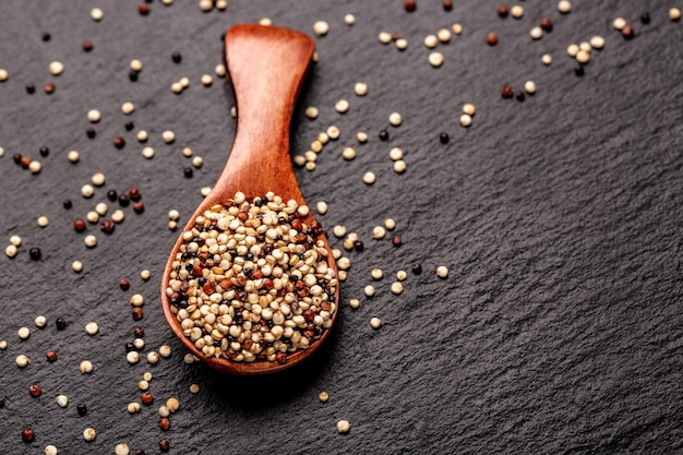 Gemischter roher unverarbeiteter Quinoa-Samen in Holzschaufel auf einem Steinhintergrund-Superfood-Produkt-Banner-Menü-Rezeptplatz für Text-Draufsicht