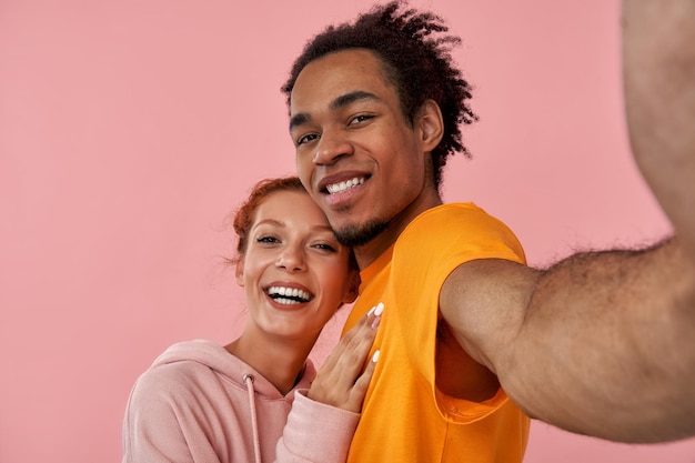Gemischtes Rassenpaar Ingwerdame schwarzes Kerlpaar machen Selfie zwinkernde Augen rosa Studiohintergrund