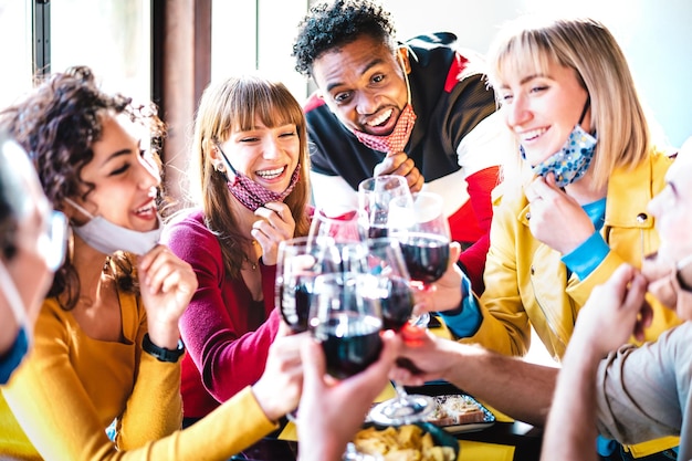 Gemischtrassige Freunde, die Rotwein in der Restaurantbar mit offener Gesichtsmaske anstoßen