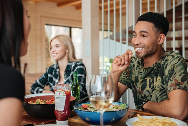 Gemischtrassige Freunde, die zu Hause am Tisch essen, trinken und reden