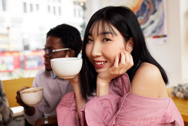 Gemischtrassige Freunde, Mädchen und Jungs, die Spaß haben, lachen, Kaffee trinken, Tee im Kaffeehaus, glückliche, vielfältige junge Leute, die reden und scherzen, sitzen zusammen am Cafétisch, multikulturelles Freundschaftskonzept