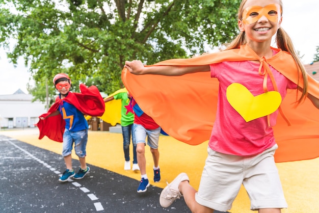 Gemischtrassige Gruppe junger Schüler, die Superheldenkostüme tragen und Spaß im Freien haben