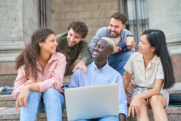 Gemischtrassige Gruppe von Studenten mit einem Laptop, die die Nachrichten besprechen