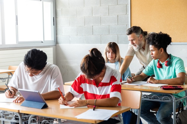 Gemischtrassige Gymnasiasten machen Hausaufgaben in der Klasse Lehrer hilft Schülern beim Unterricht Bildung