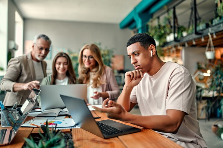 Foto gemischtrassige kreative leute im modernen büro. gruppe junger geschäftsleute und seniorchef arbeiten mit laptop, tablet, smartphone, notebook, grafiken zusammen. erfolgreiches team im coworking