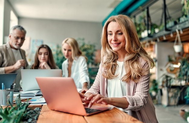 Gemischtrassige kreative Leute im modernen Büro. Gruppe junger Geschäftsleute und Seniorchef arbeiten mit Laptop, Tablet, Smartphone, Notebook, Grafiken zusammen. Erfolgreiches Team im Coworking