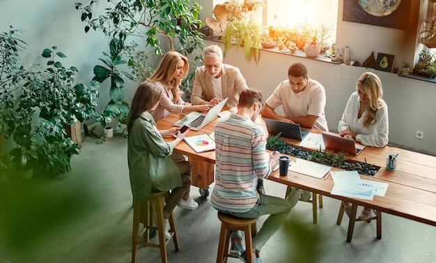 Gemischtrassige kreative Leute im modernen Büro. Gruppe junger Geschäftsleute und Seniorchef arbeiten mit Laptop, Tablet, Smartphone, Notebook, Grafiken zusammen. Erfolgreiches Team im Coworking