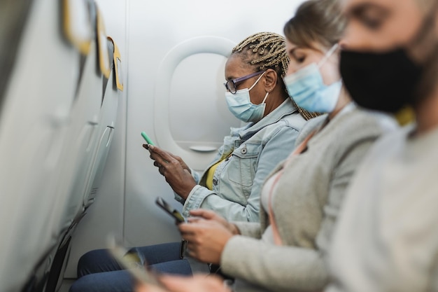 Gemischtrassige Menschen, die mit dem Handy in Flugzeugen sitzen, während sie Sicherheitsgesichtsmasken für den Ausbruch von Coronaviurs tragen