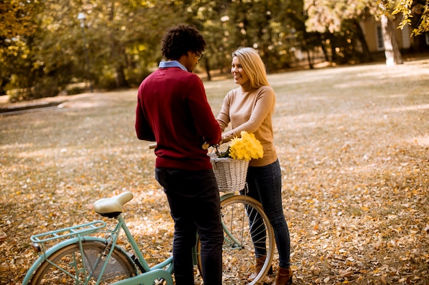Gemischtrassige Paare mit dem Fahrrad, das im Herbstpark steht