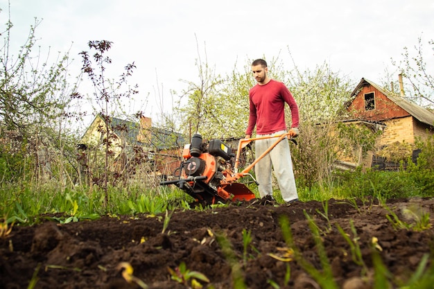 Gemüse anpflanzen unter dem handgeführten Traktor Ein Mann mit einem handgeführten Traktor im Garten Handarbeit mit Geräten Ein älterer Mann bringt einem kleinen Jungen bei, das Land zu pflügen