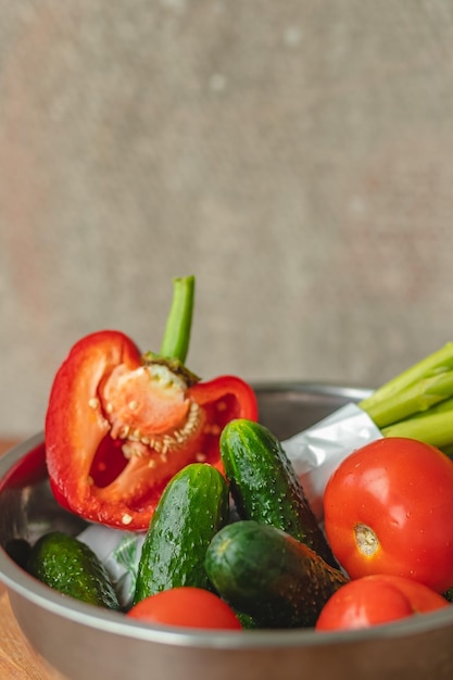 Gemüse liegen in einer Metallschüssel Tomaten Spargel Gurken rote Paprika auf einem Holzbrett und braunem Hintergrund zurück grauer Hintergrund Platz für Text